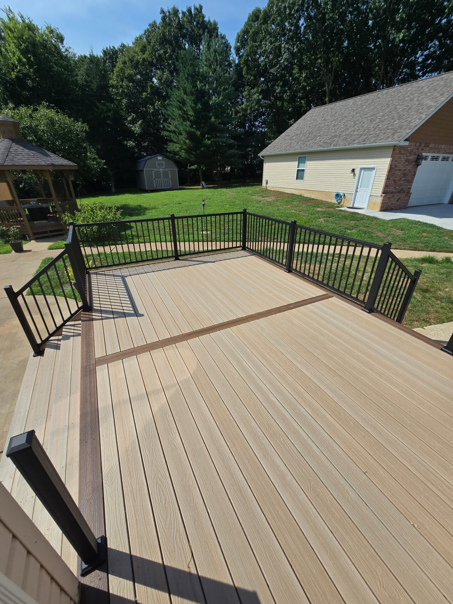 Composite deck in Rustic Auburn with a contrasting picture-frame border and center divider around a Seaside Pier field — oversized 10' stairs on the patio side by B&R Construction