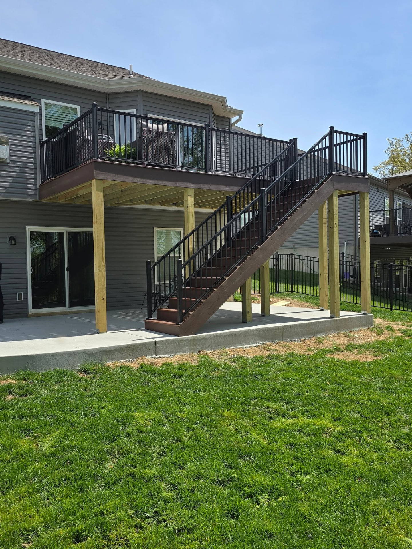 20' × 12' composite deck wrapped in Shaded Auburn with black aluminum handrails — full set of stairs, new concrete pad, and retaining walls by B&R Construction