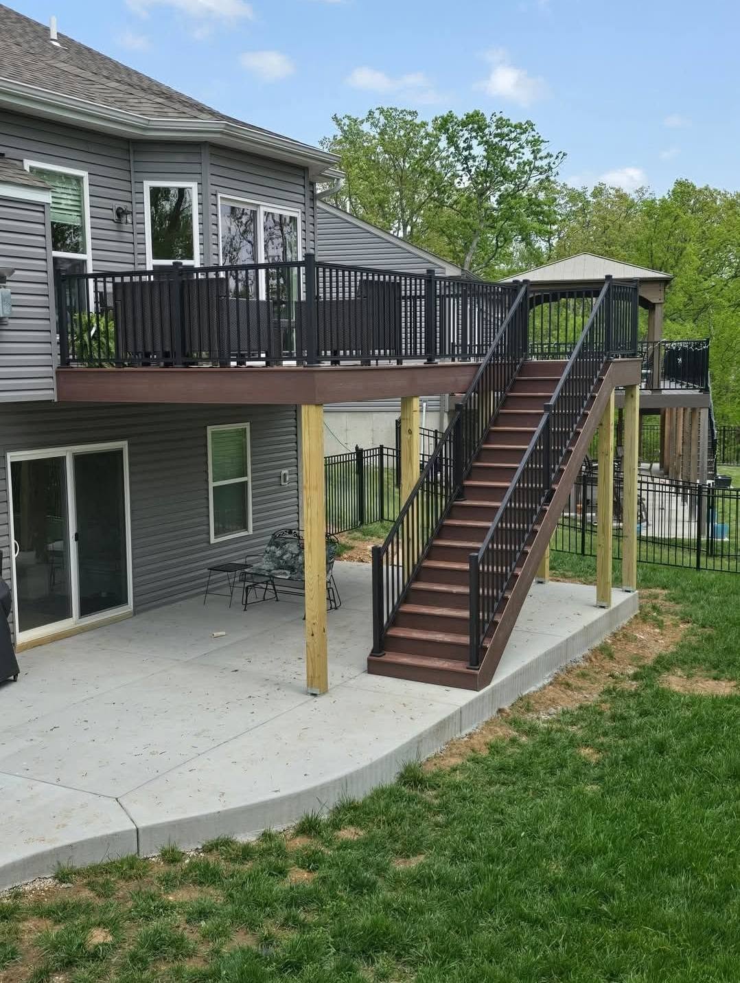 The 20' × 12' Shaded Auburn deck from the side — full stair set down to the new concrete patio on black aluminum rail by B&R Construction