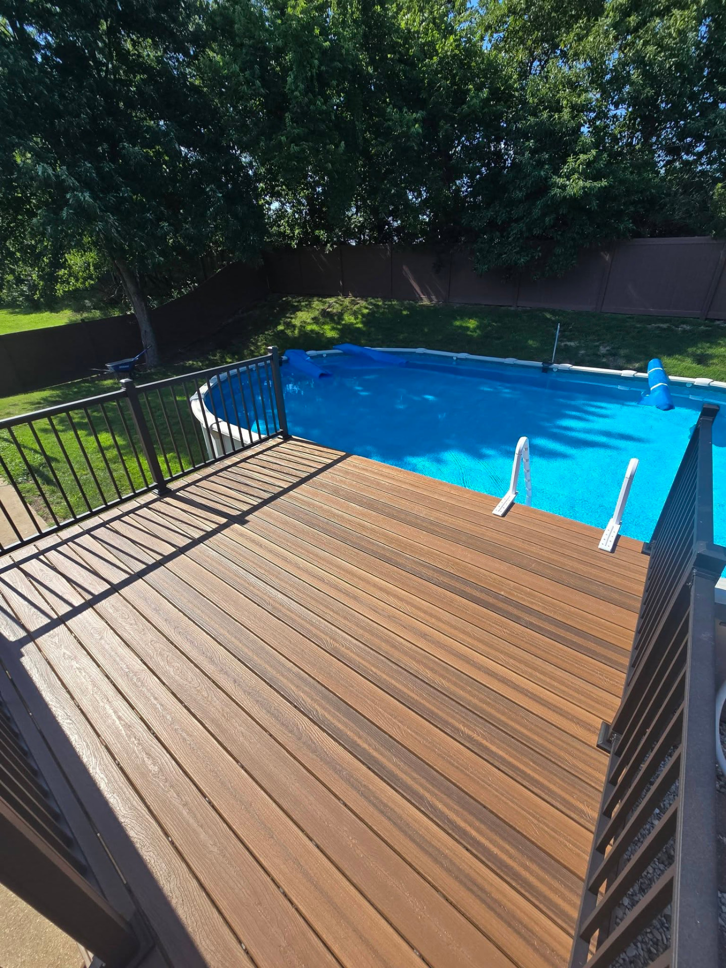 Envision Spiced Teak pool deck with black aluminum handrails, looking over the above-ground pool by B&R Construction