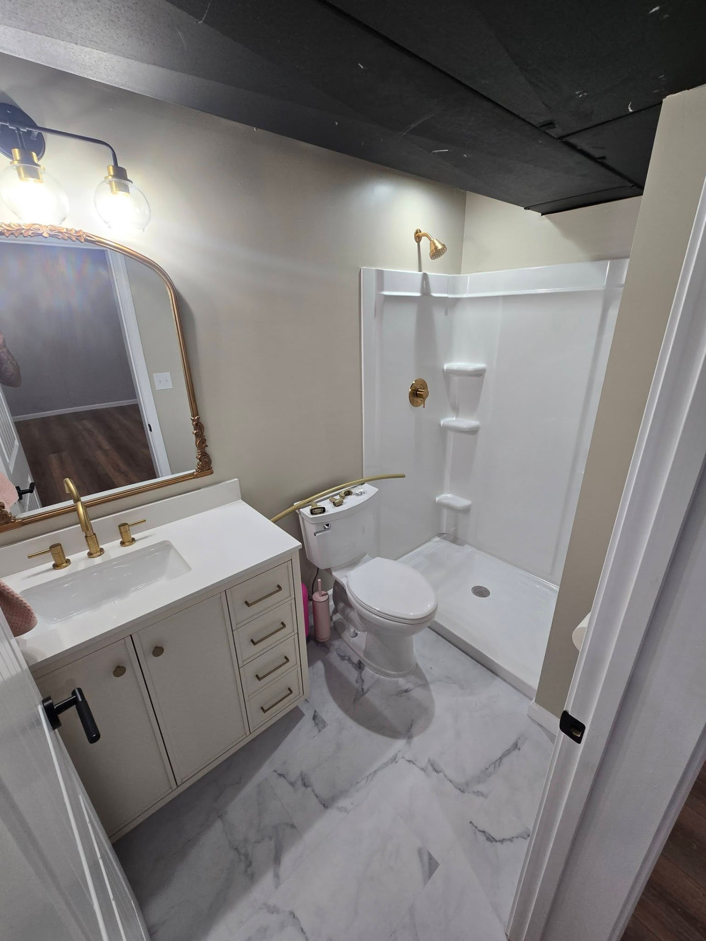 Basement bathroom with marble-look tile and gold fixtures by B&R Construction