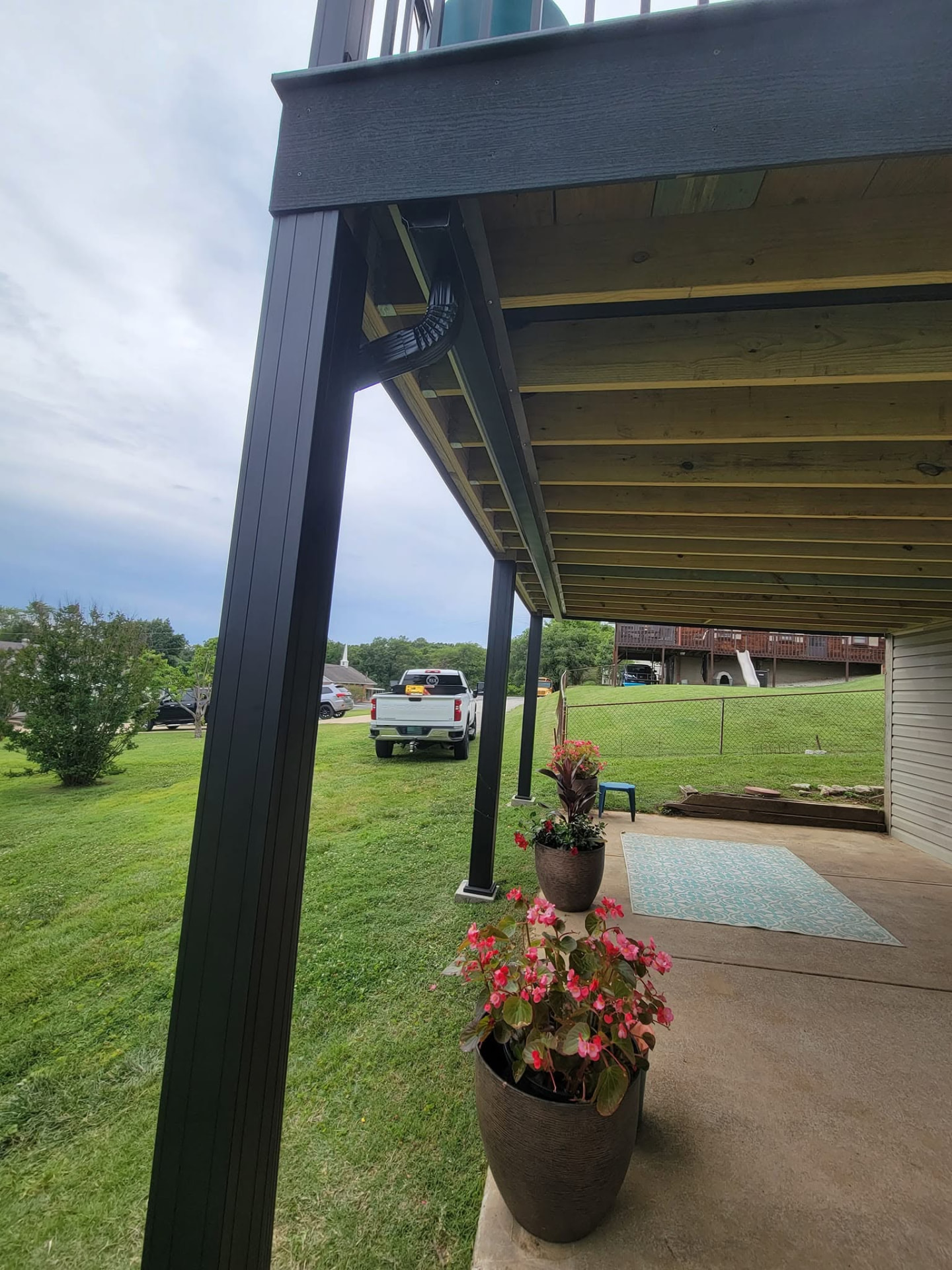 RainEscape gutter and downspout detail tucked under the deck, carrying water away from the covered patio by B&R Construction