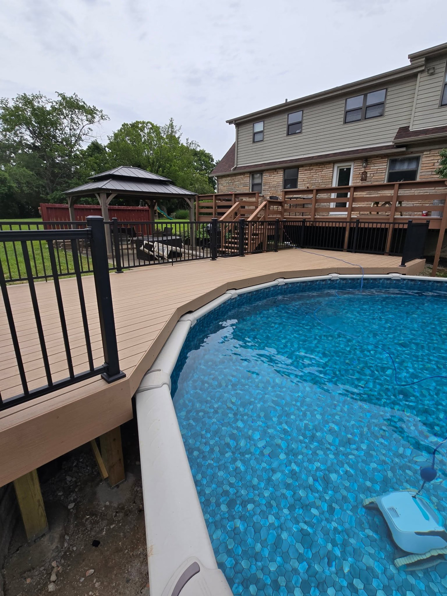 Composite pool deck alongside the pool with black aluminum handrails and the yard beyond by B&R Construction