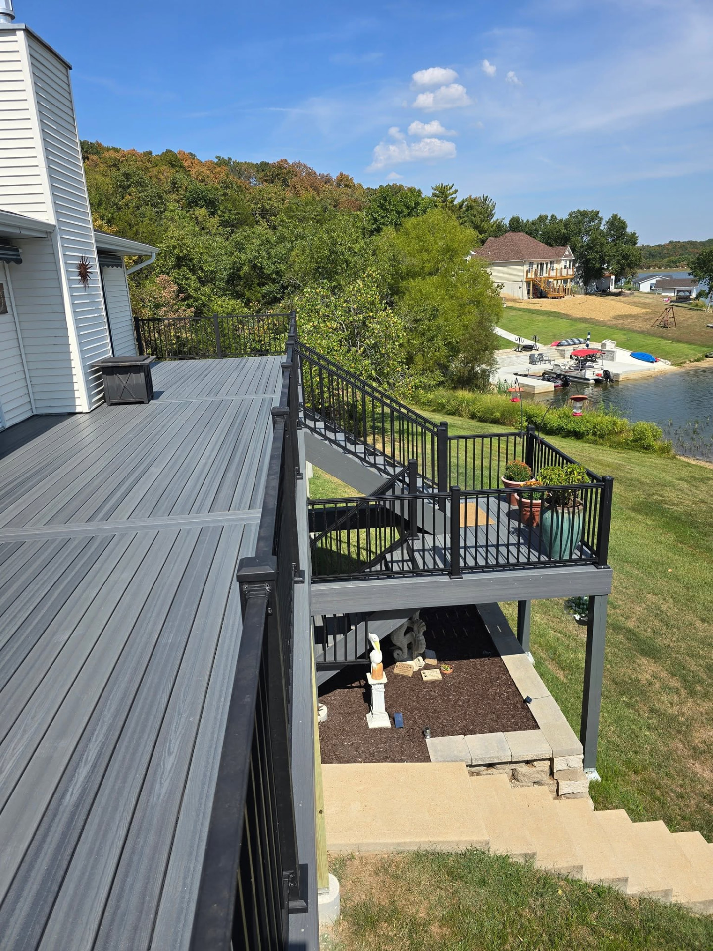 Stairs with black aluminum rail down to the lower patio on the 50' × 12' Graywood deck, with the lake in the background by B&R Construction
