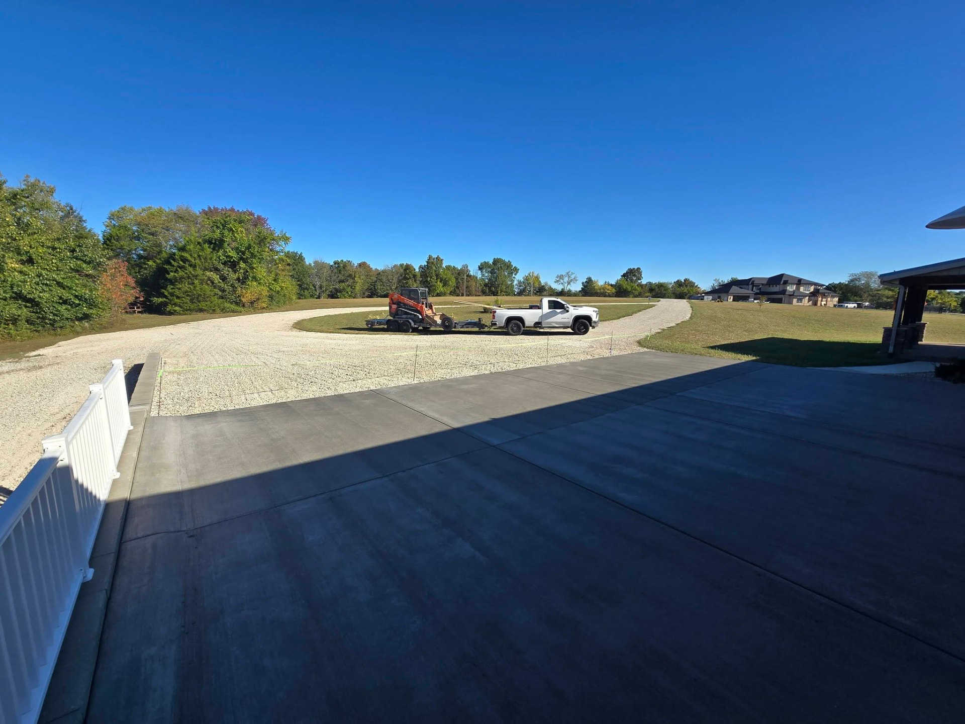 Fresh broom finish concrete pad curing, with the gravel drive and white rail beyond by B&R Construction
