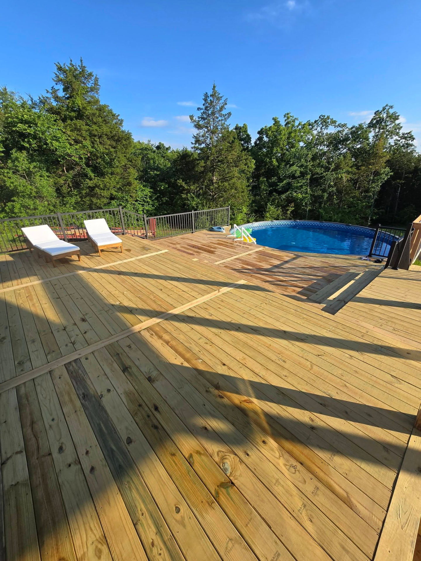 New treated pool deck with black aluminum handrails built around the above-ground pool by B&R Construction