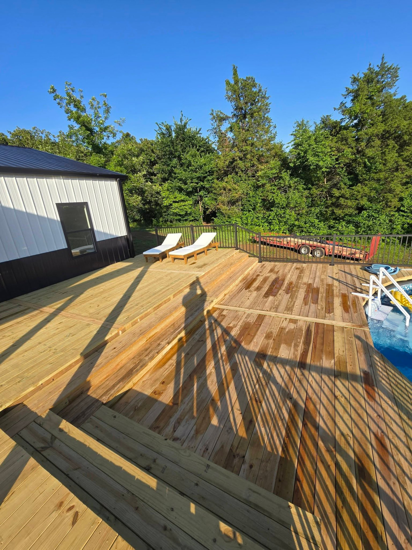 Fresh treated decking wrapping the above-ground pool with black aluminum handrails and pool stairs by B&R Construction