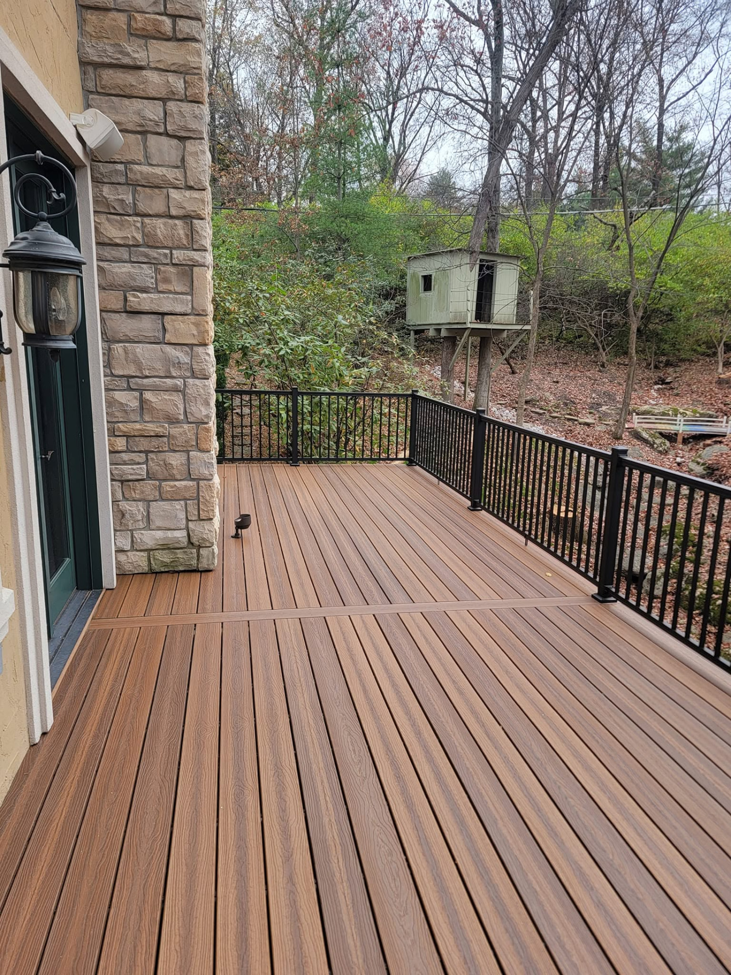 Fresh Spiced Teak composite decking with black aluminum handrails overlooking the wooded lot by B&R Construction