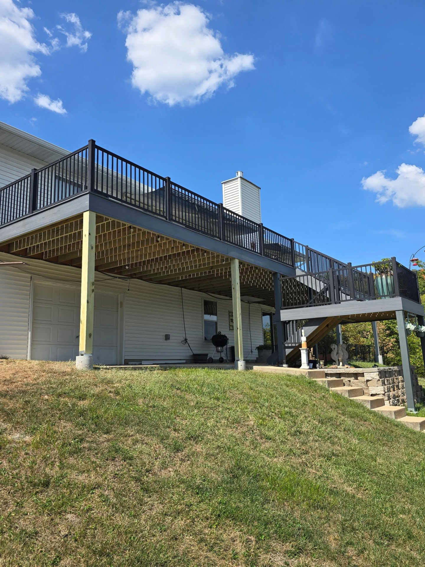 The 50' × 12' Graywood deck from the yard — second-story deck over the walkout with picture-frame borders and black aluminum handrails by B&R Construction
