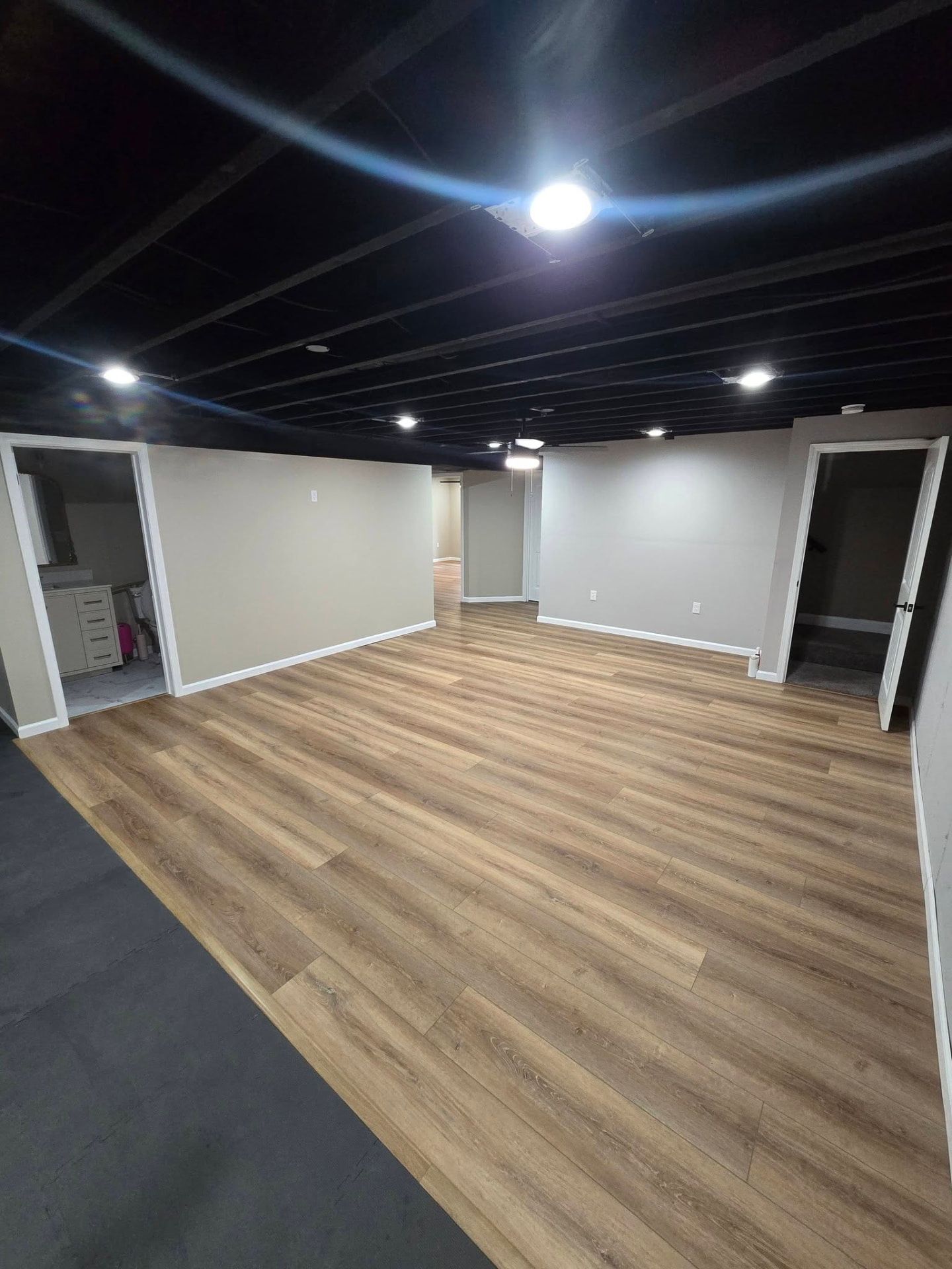 Open basement living area — black-painted ceiling, can lights, and LVP flooring by B&R Construction