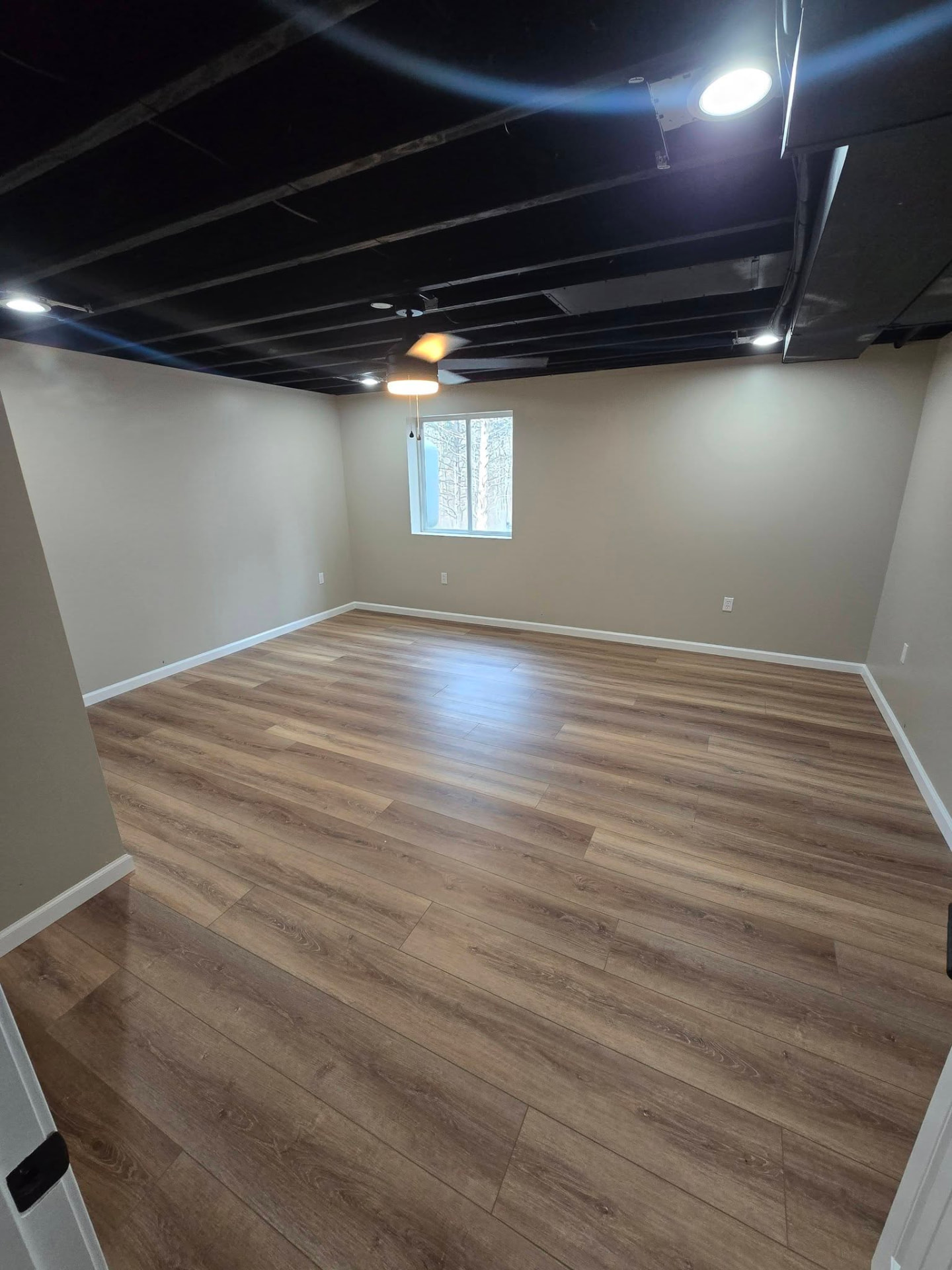 Basement living room with a black-painted ceiling and LVP floors by B&R Construction