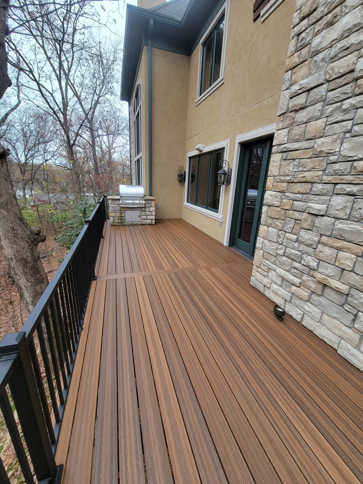 Spiced Teak composite boards and black aluminum rail beside the stone grill island by B&R Construction