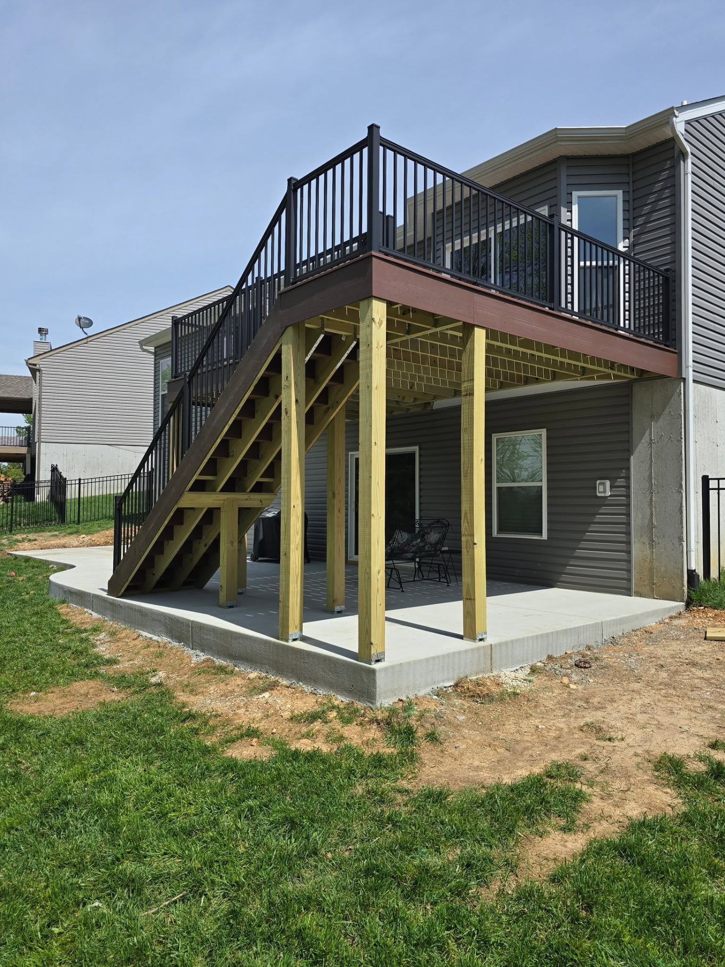 Oversized stairs on the Shaded Auburn deck landing on the new concrete pad, with retaining walls holding the grade by B&R Construction