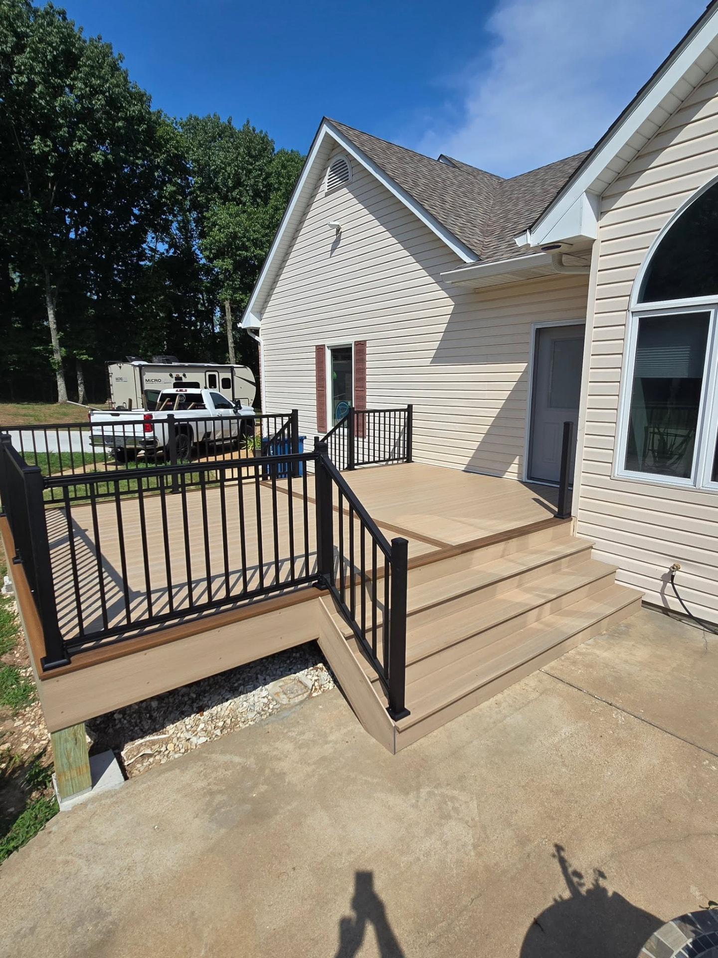 Oversized 10' stairs on the patio side of the Rustic Auburn composite deck, with black aluminum handrails down to the concrete patio by B&R Construction