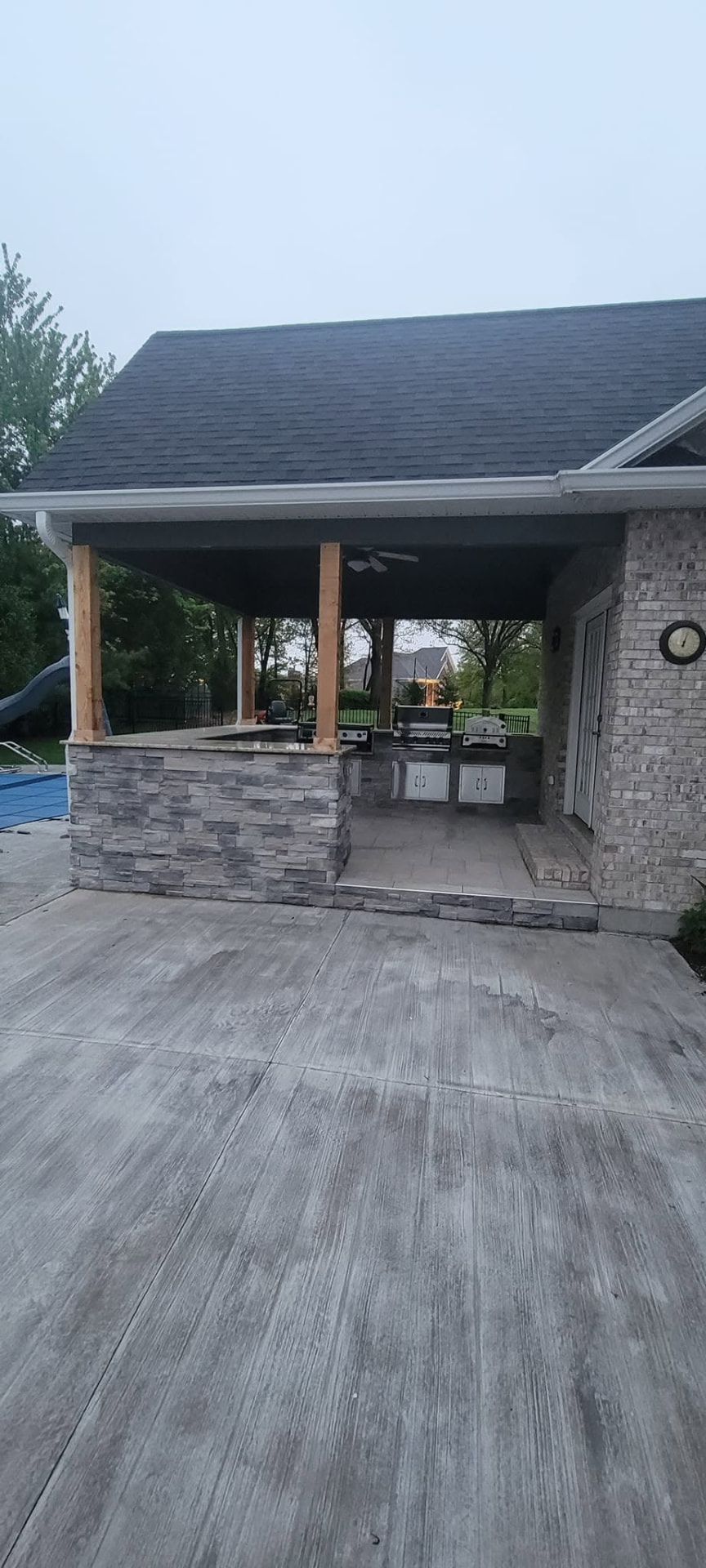 The outdoor kitchen's stone bar and covered patio from the driveway, with the grill station on the house wall by B&R Construction