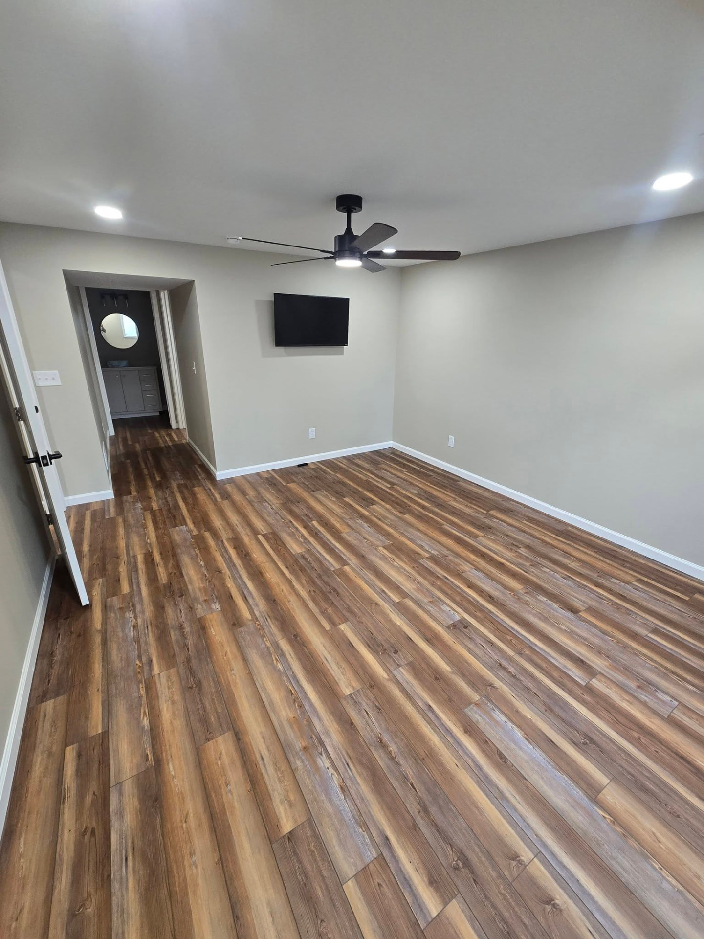 Basement bedroom with LVP flooring, ceiling fan, and wall-mounted TV by B&R Construction