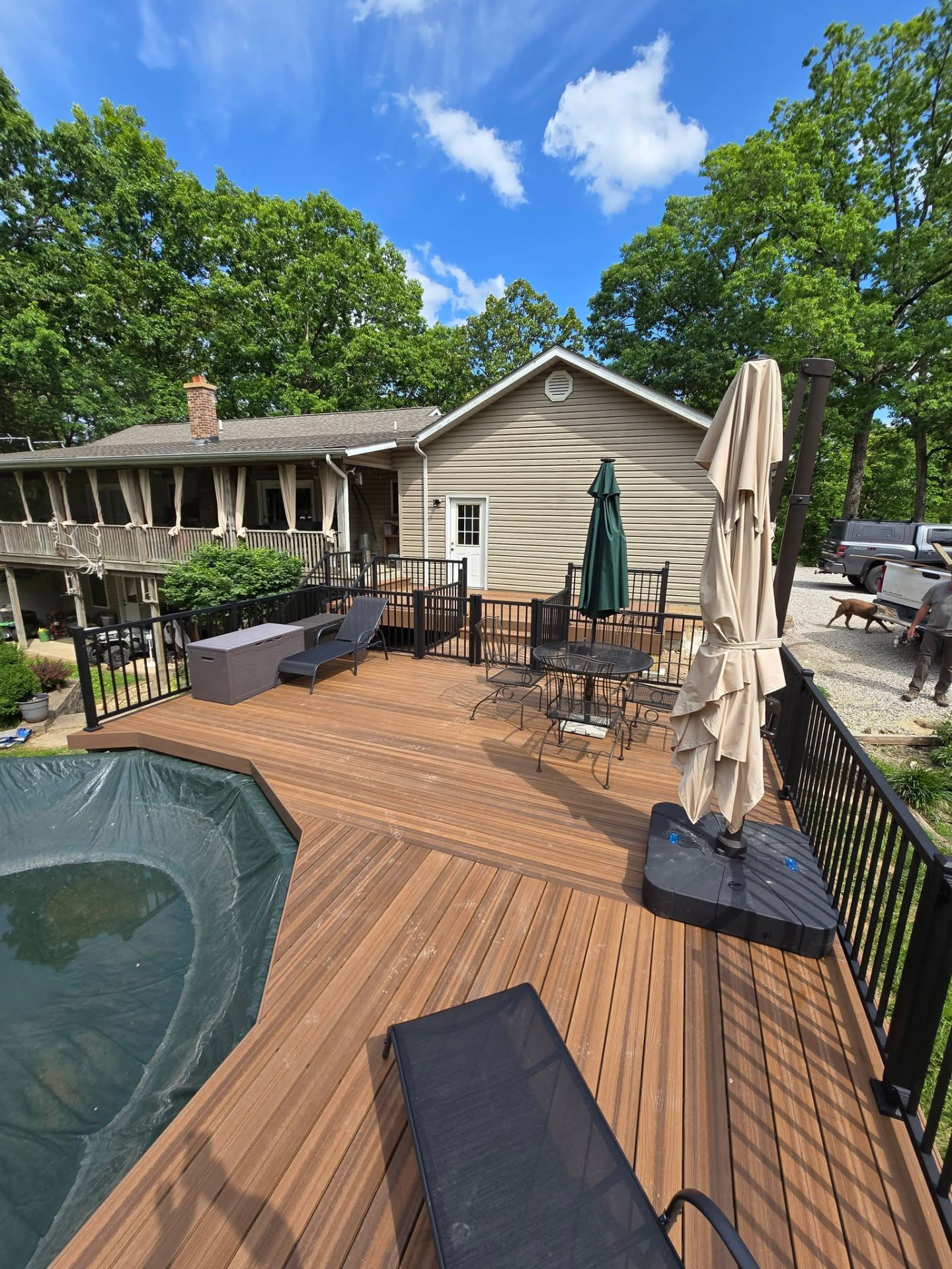 Multi-level composite pool deck with black aluminum handrails wrapping the above-ground pool, with the covered porch and grill area off the house by B&R Construction
