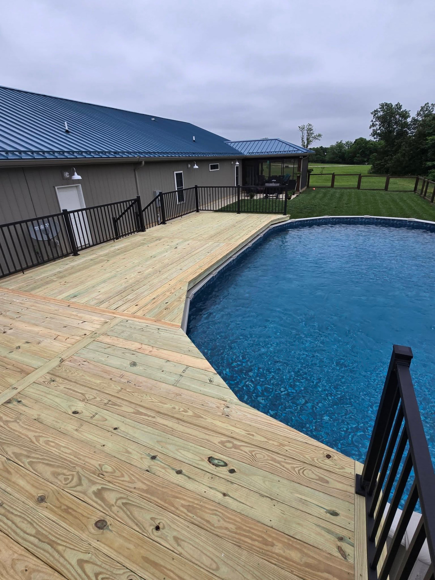 450 sq ft above-ground pool deck — treated framing and decking, screwed down, wrapped in black aluminum handrails by B&R Construction