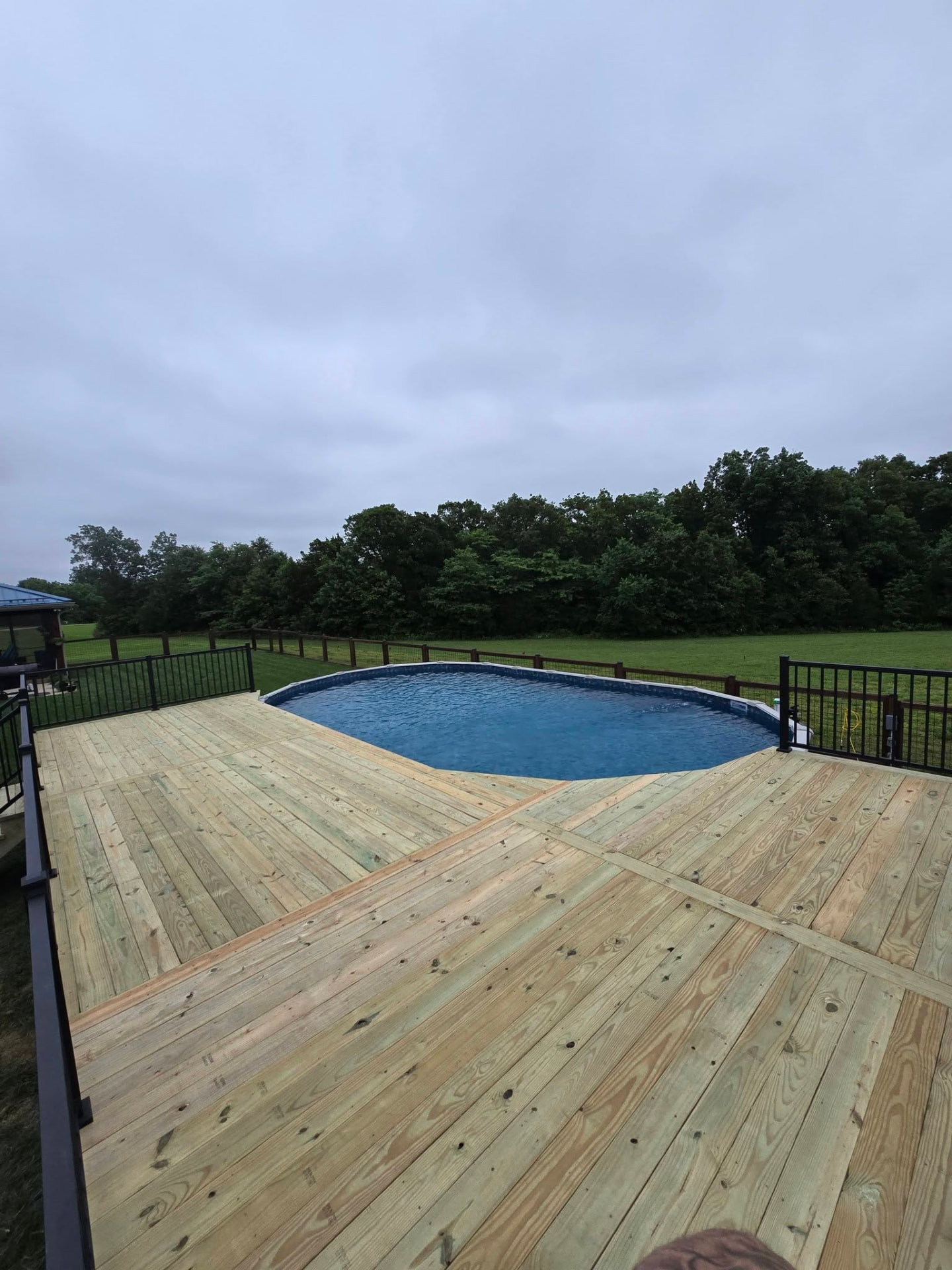 Treated pool deck wrapping the pool with black aluminum handrail by B&R Construction
