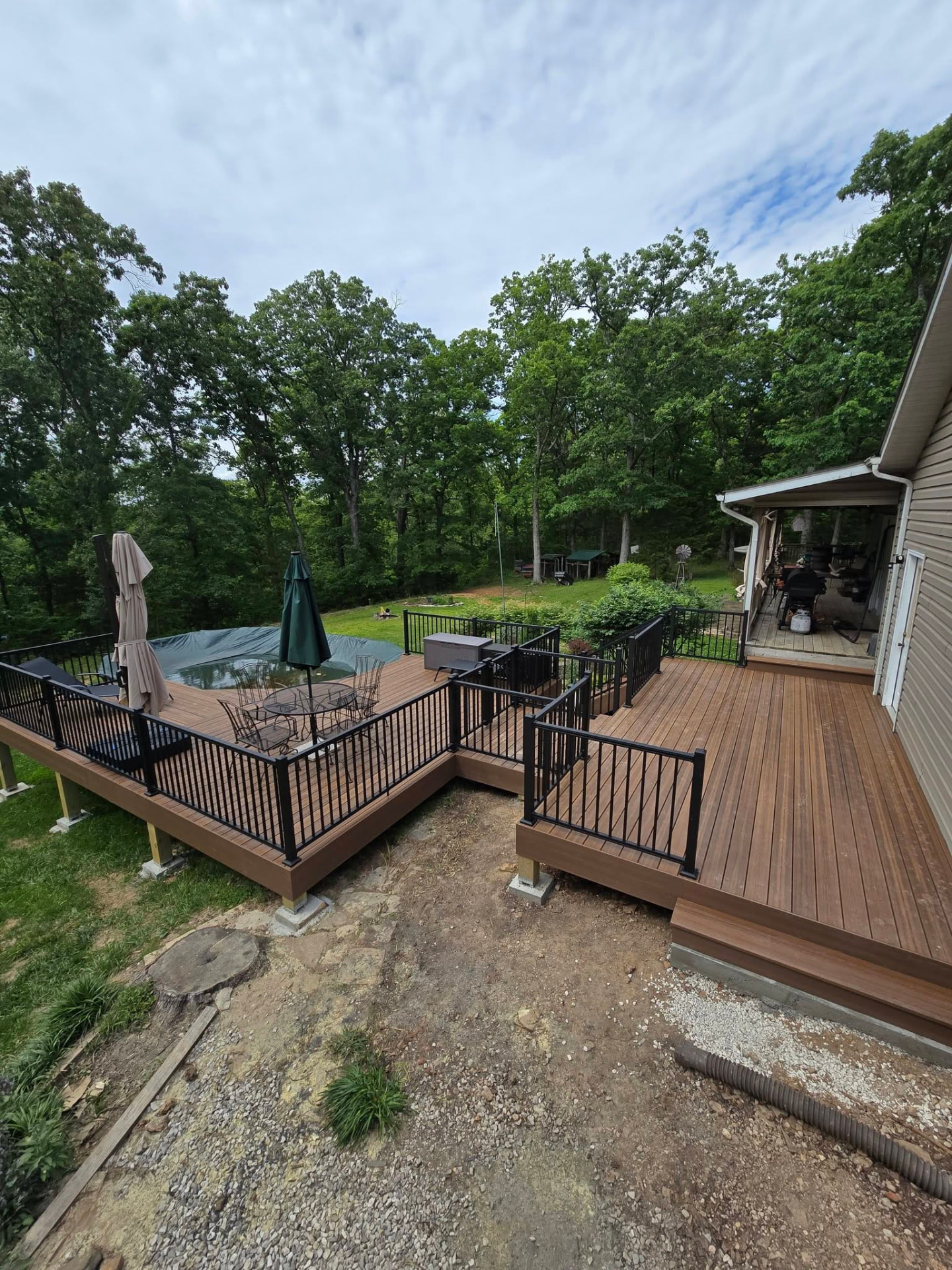 The full pool deck from above — two connected composite levels with black aluminum handrails, stairs, and lounge space around the pool by B&R Construction