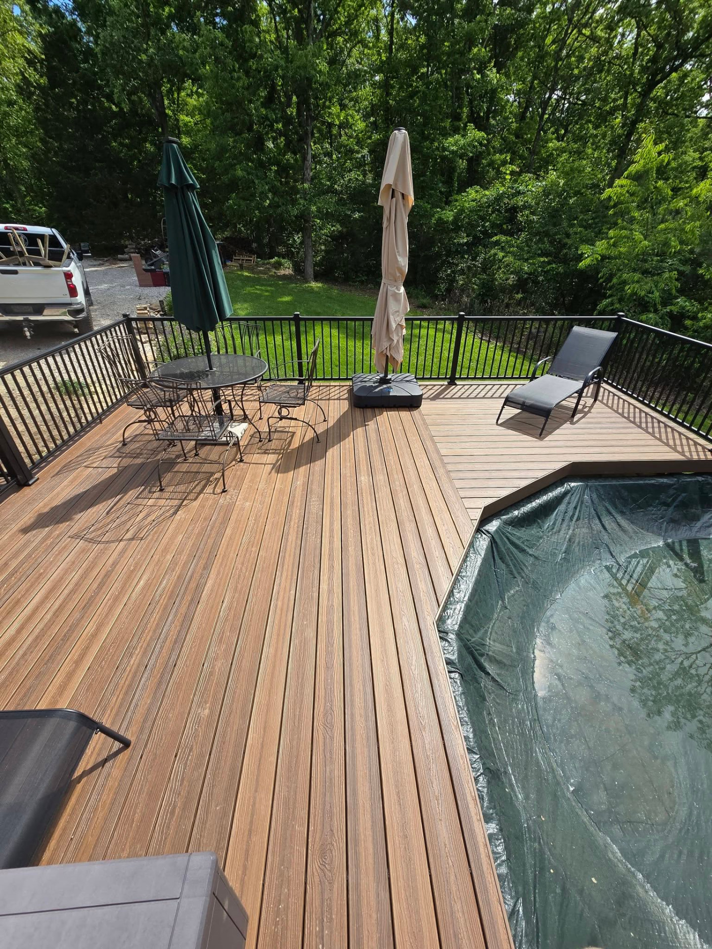 Maintenance-free composite boards with black aluminum handrails around the pool — table, umbrellas, and loungers on deck by B&R Construction